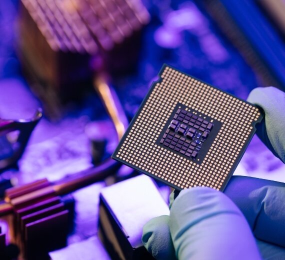 Close up of an engineer holding a computer microchip with a motherboard in the background
